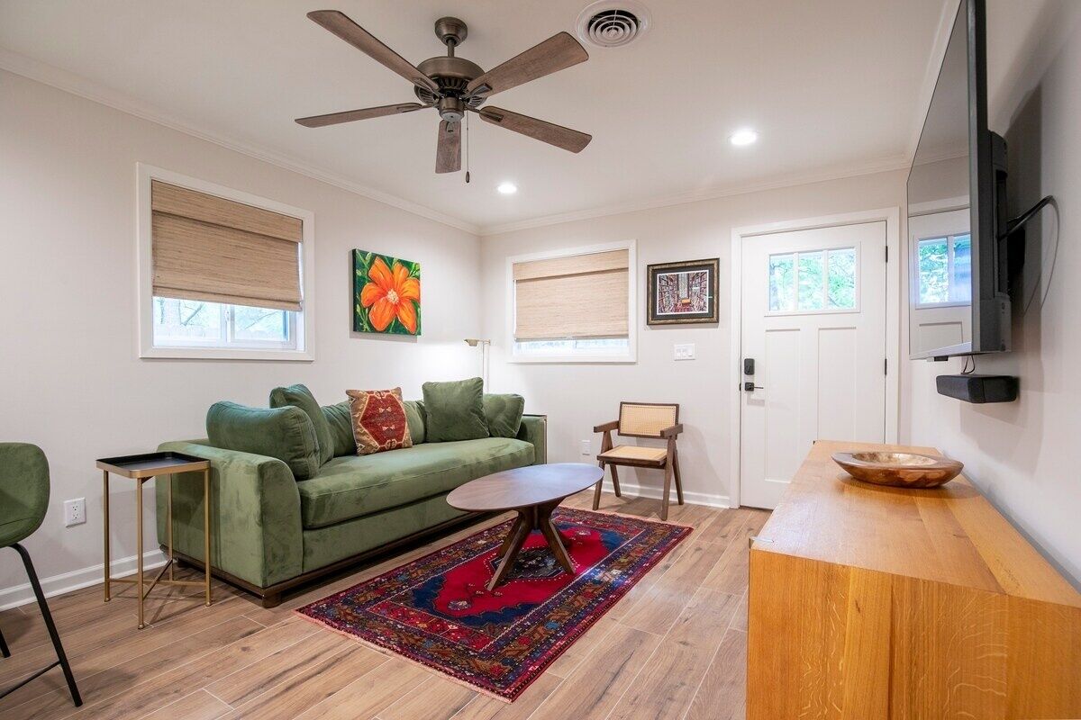A living room with a green sofa, a wooden coffee table, a ceiling fan, and a television on the wall.