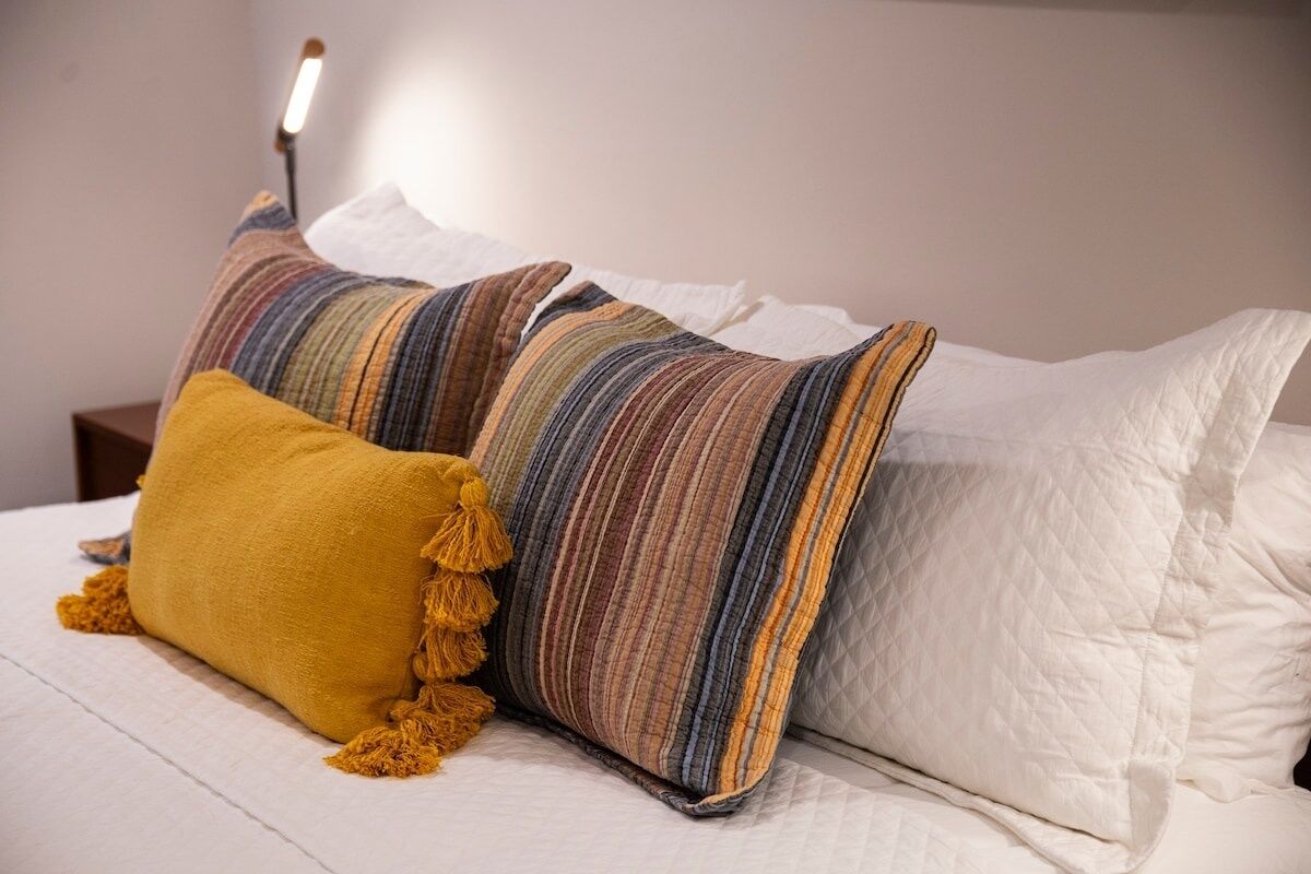 Een bed met witte lakens, een geel kussen en gestreepte kussens.