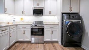 A modern kitchen with white cabinets, stainless steel appliances, and a built-in washer and dryer.