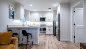 A modern kitchen with white cabinets, a central island, bar stools, a sofa, and a refrigerator.