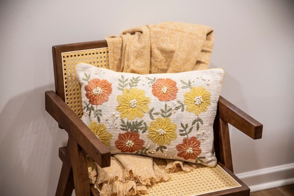 Une chaise en bois avec un dossier en osier et un coussin orné d’un motif floral.