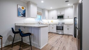 A modern kitchen with white cabinets, a central island, bar stools, stainless steel appliances, and a painting on the wall.