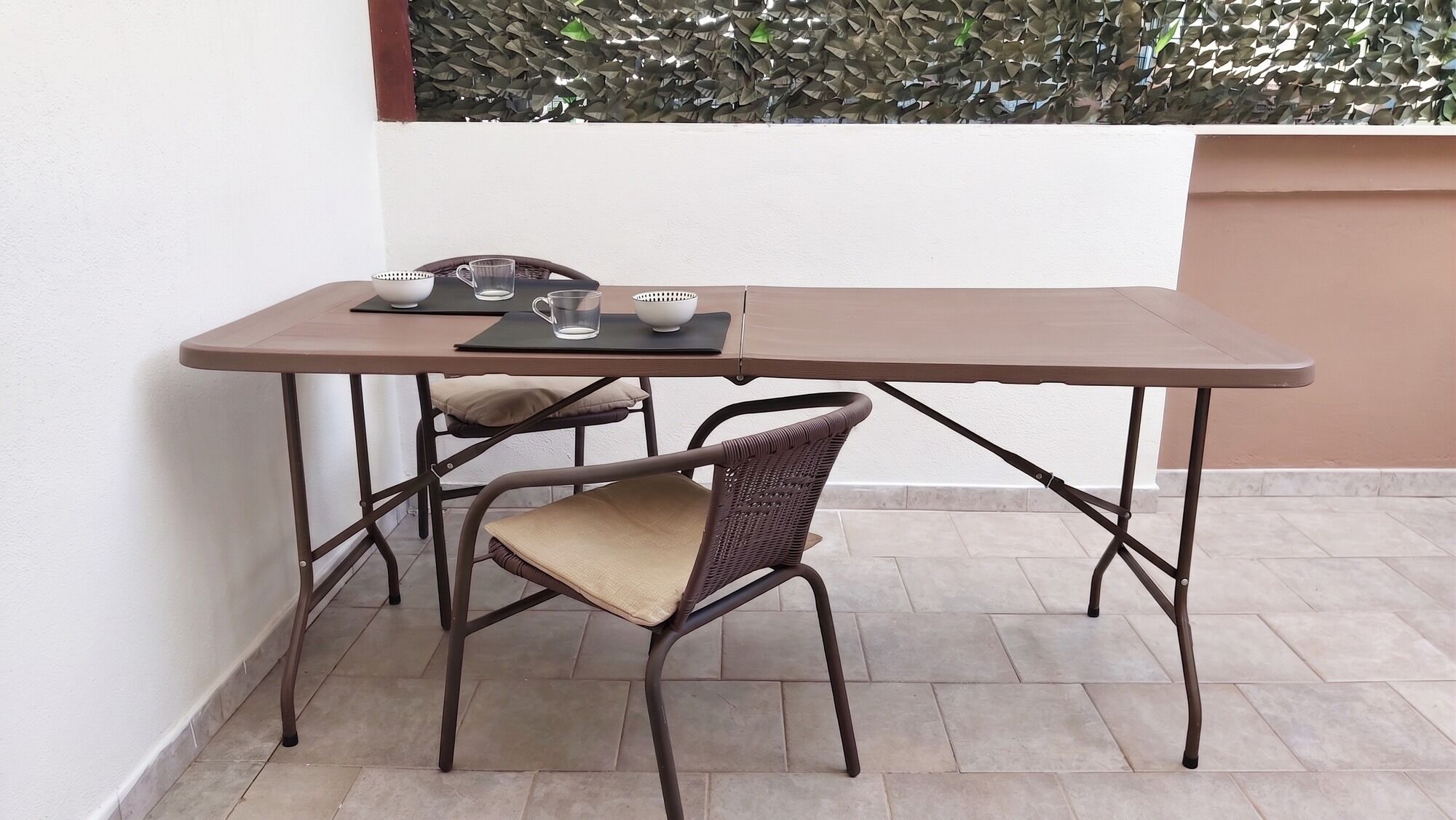 Una pequeña mesa exterior con dos sillas, estructura metálica y cojines.