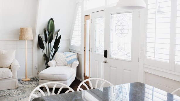 A bright, white interior with a dining area, two white chairs, a table, a floor lamp, and a large plant. - A-Frame - 2 minute walk to Beach - Pet Friendly - HUGE front and back porch (Carolina Beach)