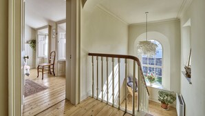 Un'ampia sala con pavimento in legno, una scala bianca e vista su una zona pranzo con una sedia e un tavolo.