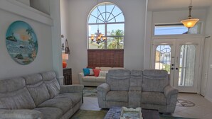 Ein Wohnzimmer mit zwei grauen Sofas, einem Couchtisch und einem großen Fenster mit Blick auf Palmen.