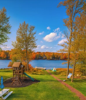 Une aire de jeux au bord du lac, avec une cabane en bois, des toboggans et des tables de pique-nique.