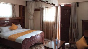A hotel room with a large bed, a wooden headboard, a bedside table, and a wardrobe. - Sweet Bargain Hotel (Nakuru)