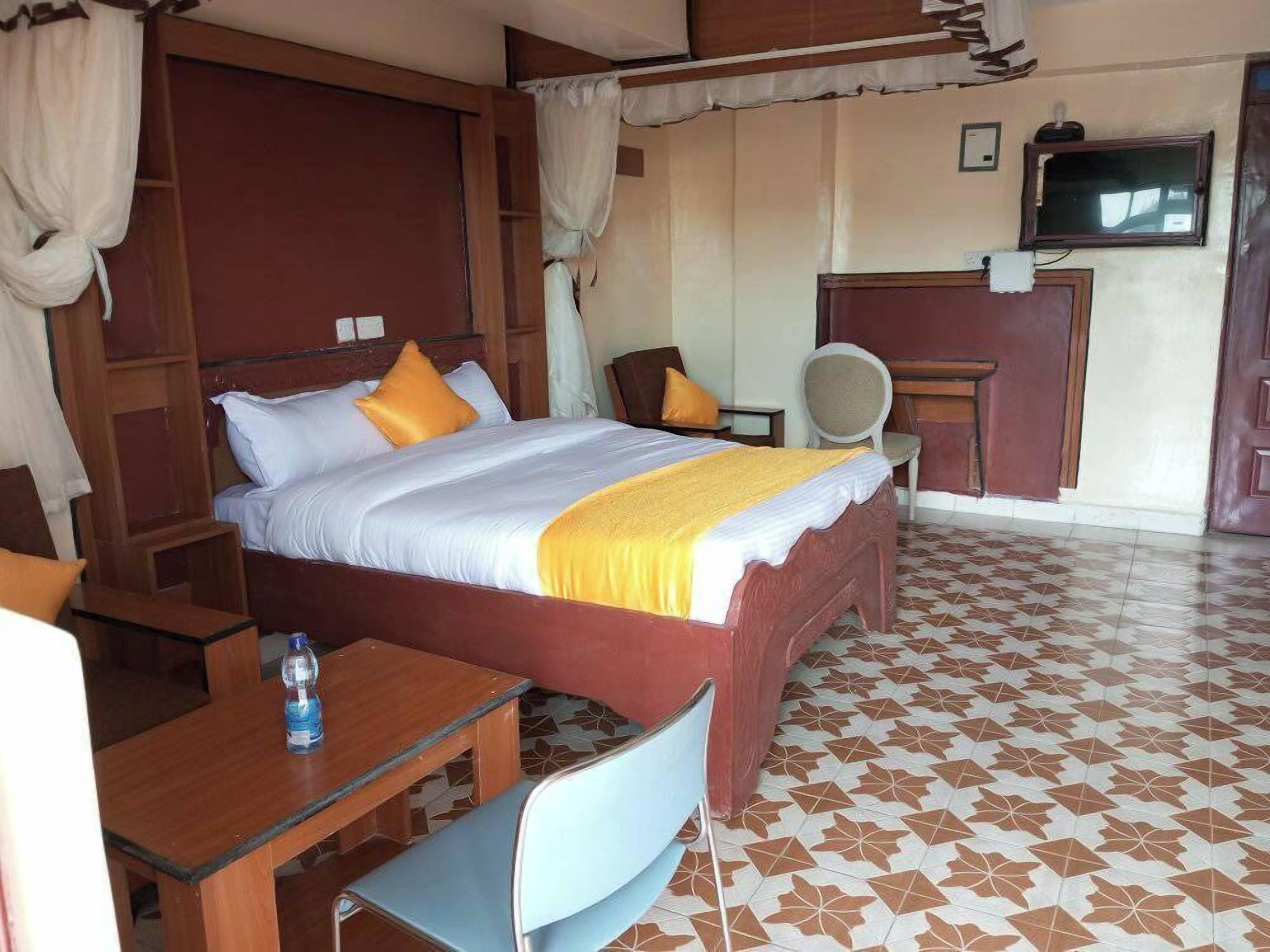 A hotel room with a bed, a desk, a chair, a TV, and a bathroom.