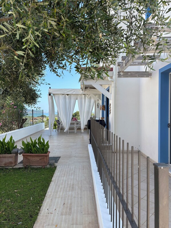 A covered outdoor area with a wooden deck, white curtains, and potted plants.