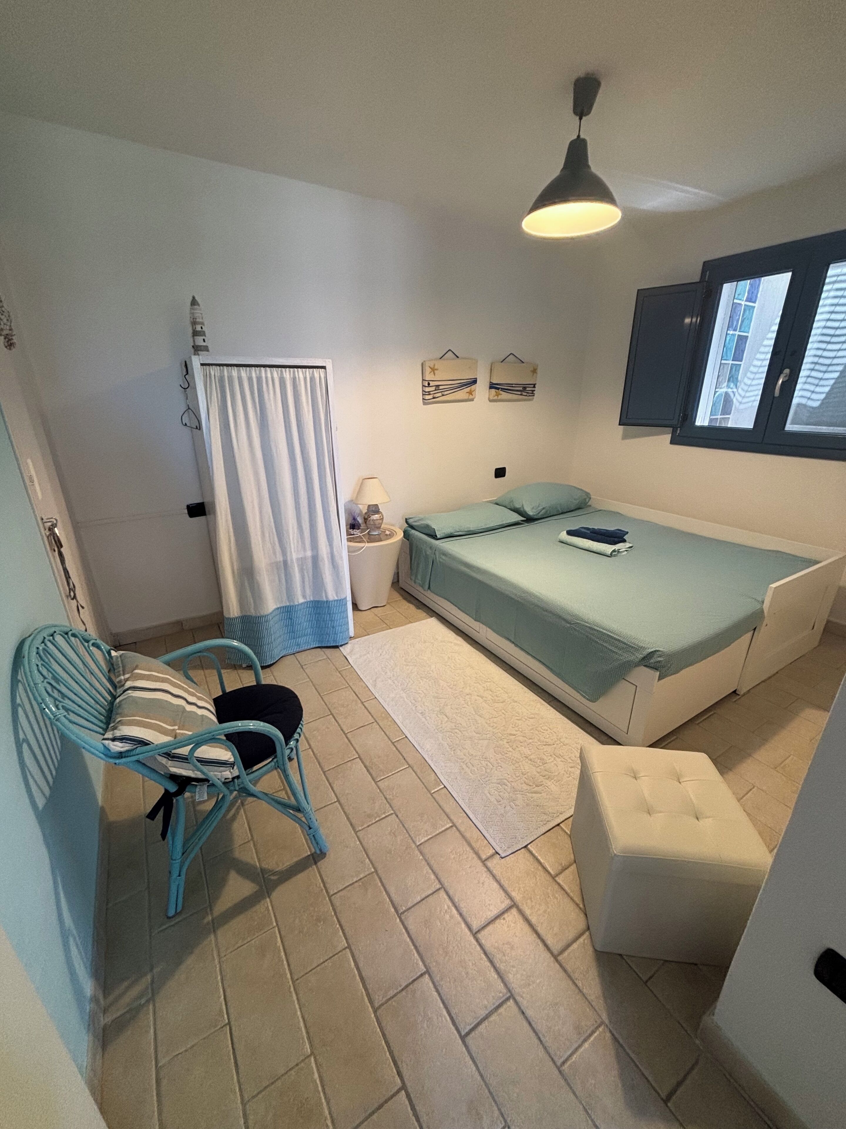Une petite pièce bien éclairée, avec un lit, une chaise, une petite table et une fenêtre.