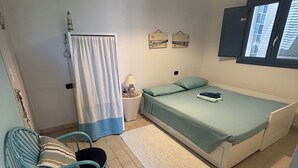 Une petite pièce bien éclairée, avec un lit, une chaise, une petite table et une fenêtre.