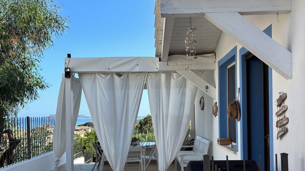 Un espace extérieur abrité, agrémenté de rideaux blancs, d’un barbecue et offrant une vue sur la mer.