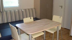 Una habitación con una mesa de madera, cuatro sillas, un banco a rayas y un armario.