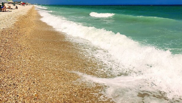 Una playa con agua turquesa cristalina, orilla pedregosa y sombrillas.