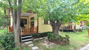 Una casa amarilla con porche, un árbol en frente y un pequeño jardín.