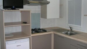 Cocina compacta con estufa a gas, horno empotrado, microondas y televisor sobre una repisa.
