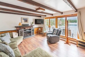 Una sala de estar con chimenea, un conjunto de sofás, un televisor y vistas a un lago a través de amplios ventanales.