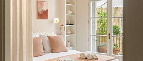 Une chambre d’hôtel comprenant un lit, des oreillers, une lampe de chevet, une fenêtre donnant sur l’extérieur et une étagère avec des objets décoratifs.