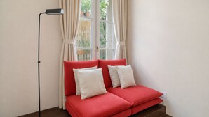 A red sofa with white cushions, a floor lamp, and a window with curtains. - 1538 Visconti (Paris)