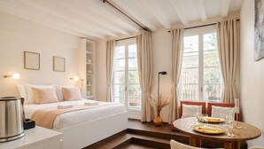 A hotel room with a bed, bedside table, lamp, dining table with chairs, and a window with curtains. - 1538 Visconti (Paris)