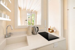 Une salle de bain moderne avec un lavabo blanc, une bouilloire et un miroir qui reflète une fenêtre donnant sur un espace verdoyant.