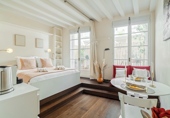 Relax in a serene space with a large bed, seating area, and desk, offering a view of the outdoors.
