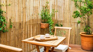 A wooden table with a tray, two white cups, and a potted plant against a bamboo fence. - 1538 Visconti (Paris)