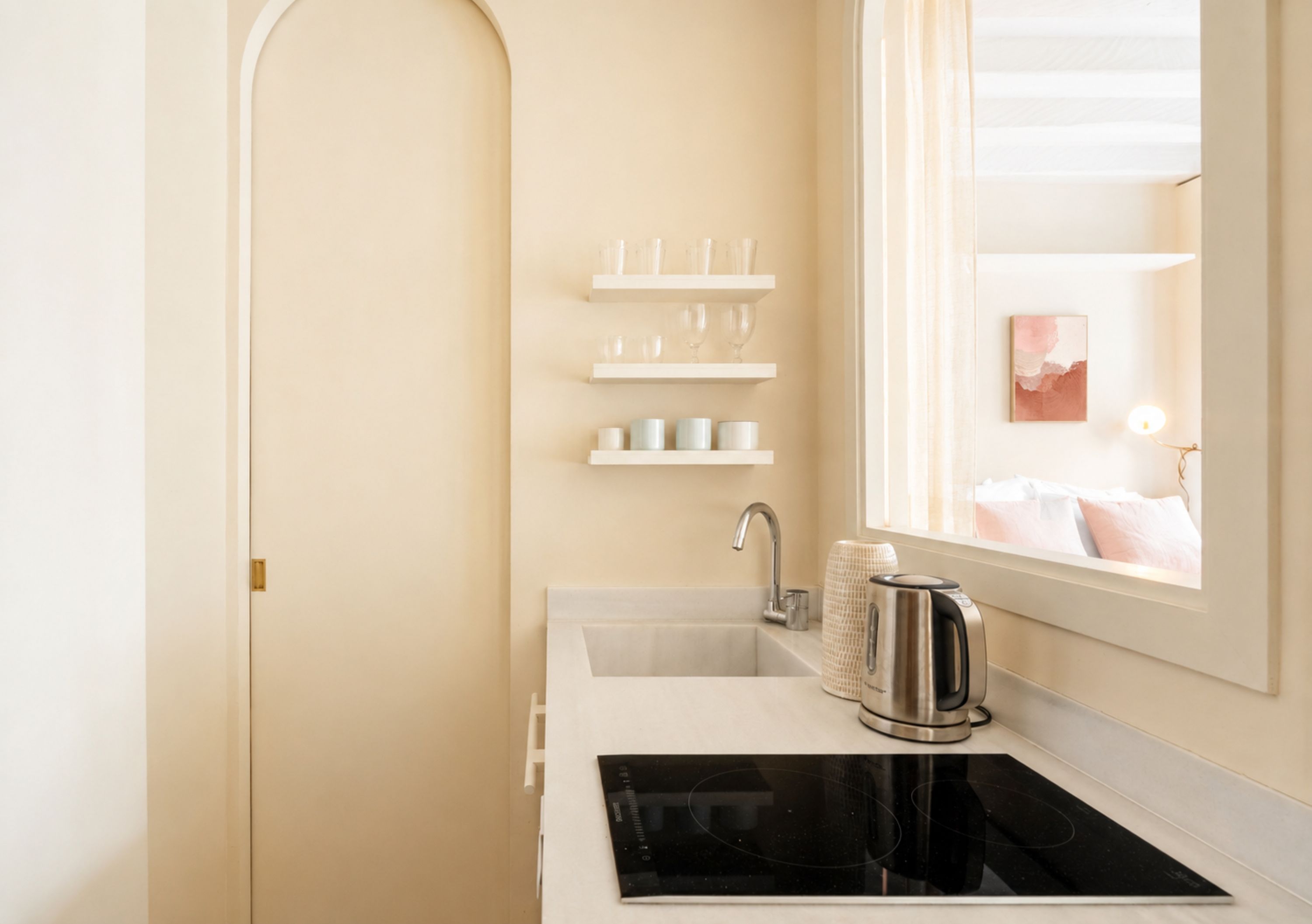 A modern kitchen with a black countertop, white cabinetry, and a window with a view of a bedroom.