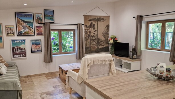 A cozy living room with a sofa, a coffee table, a TV, and a dining area with a wooden table and chairs.