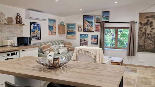 Un salón acogedor con un sofá, una mesa de centro y una mesa de comedor. Hay cuadros en la pared y un ventanal con cortinas.