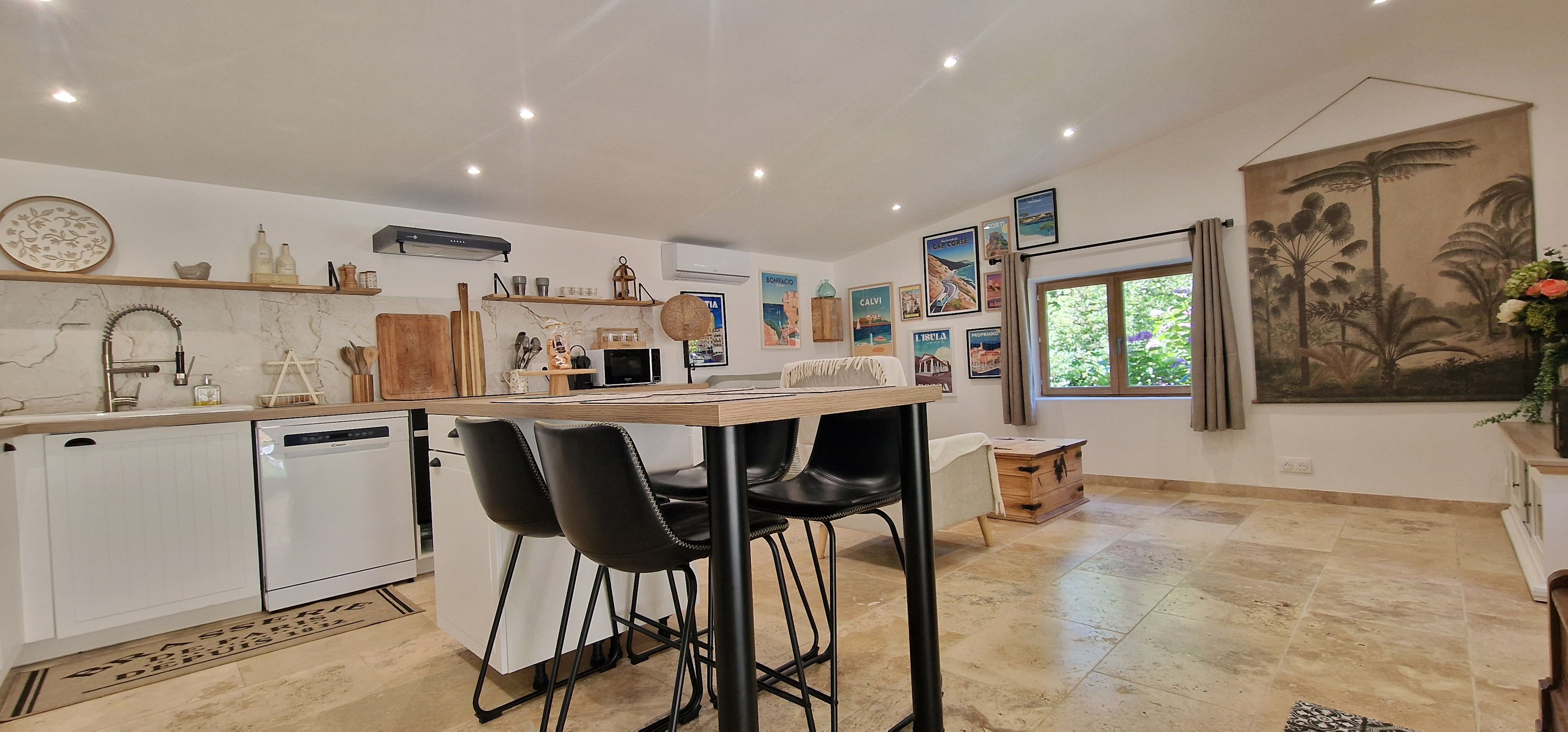 A modern kitchen with white cabinetry, a dining area with black chairs, and a large window with a view of greenery.