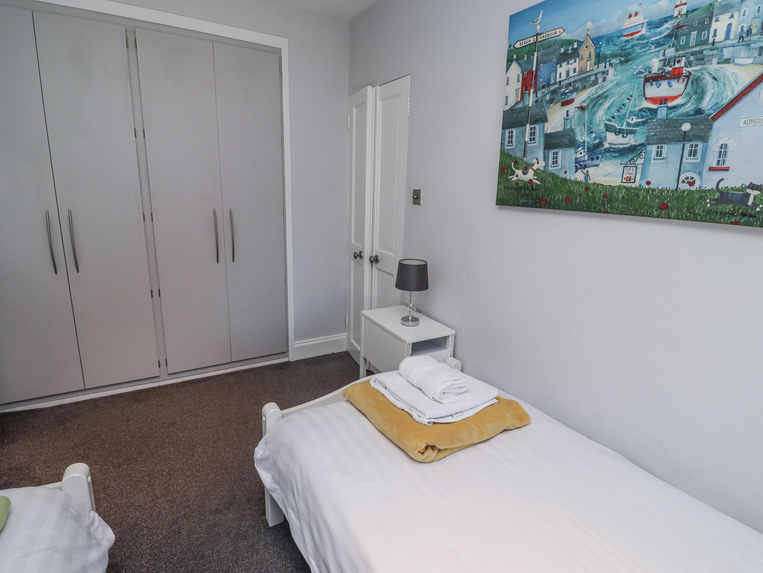 A bedroom with a bed, a nightstand, a lamp, a painting, and a wardrobe.