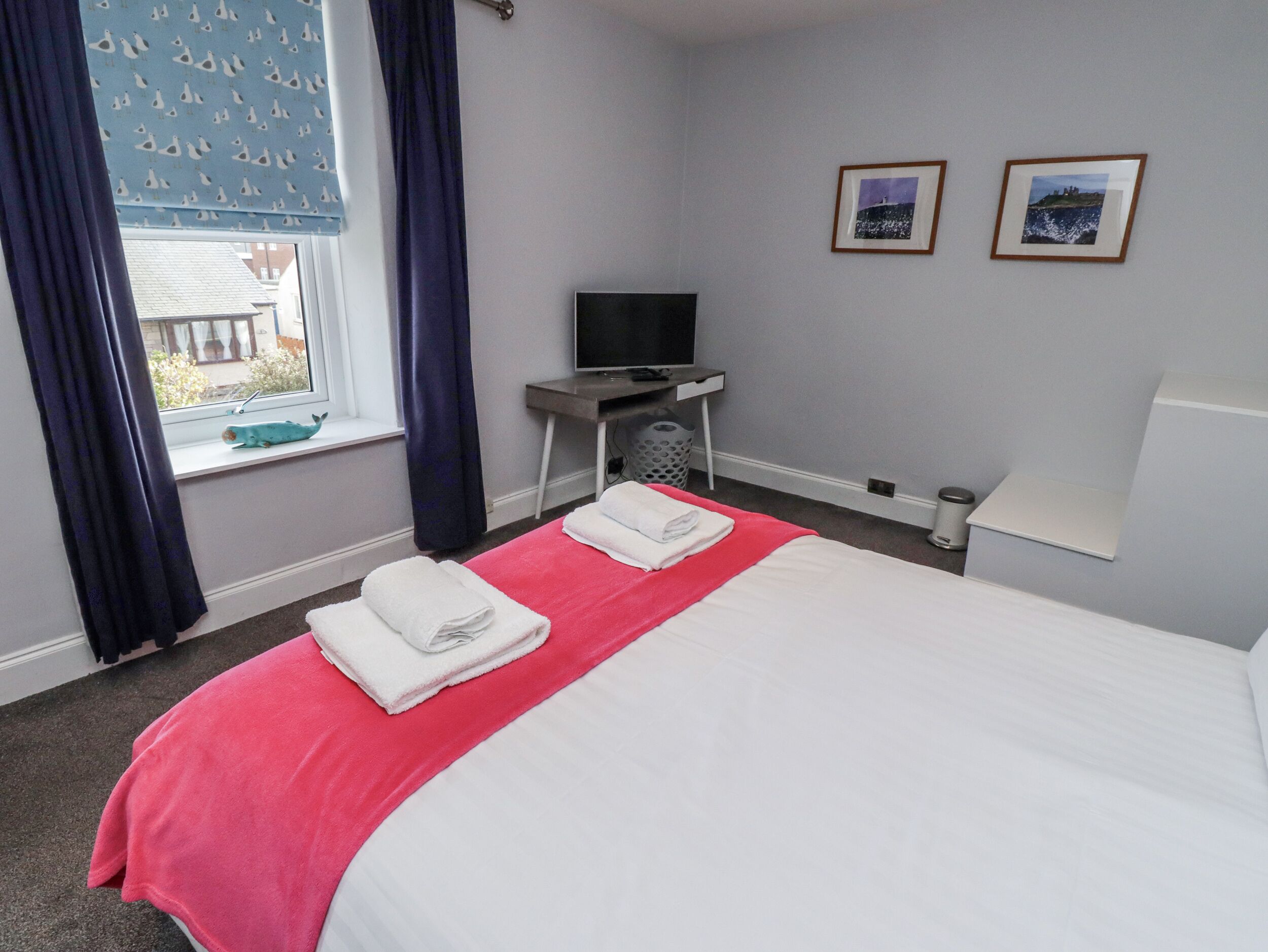 Ein Hotelzimmer mit einem Bett, einem Schreibtisch mit Fernseher und zwei gerahmten Bildern an der Wand.