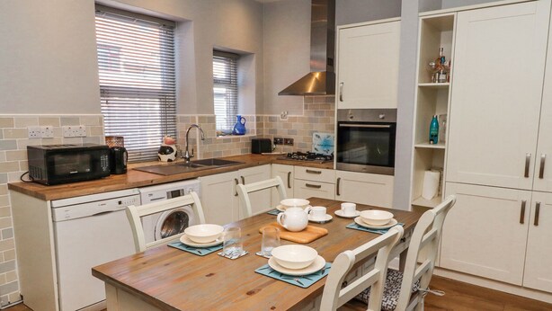Una cocina moderna con una mesa de madera dispuesta para comer, armarios blancos e horno empotrado.