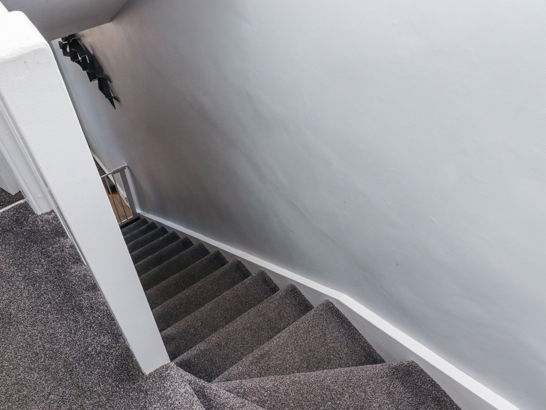 Un escalier dont les marches sont recouvertes de moquette et qui possède une rampe blanche.