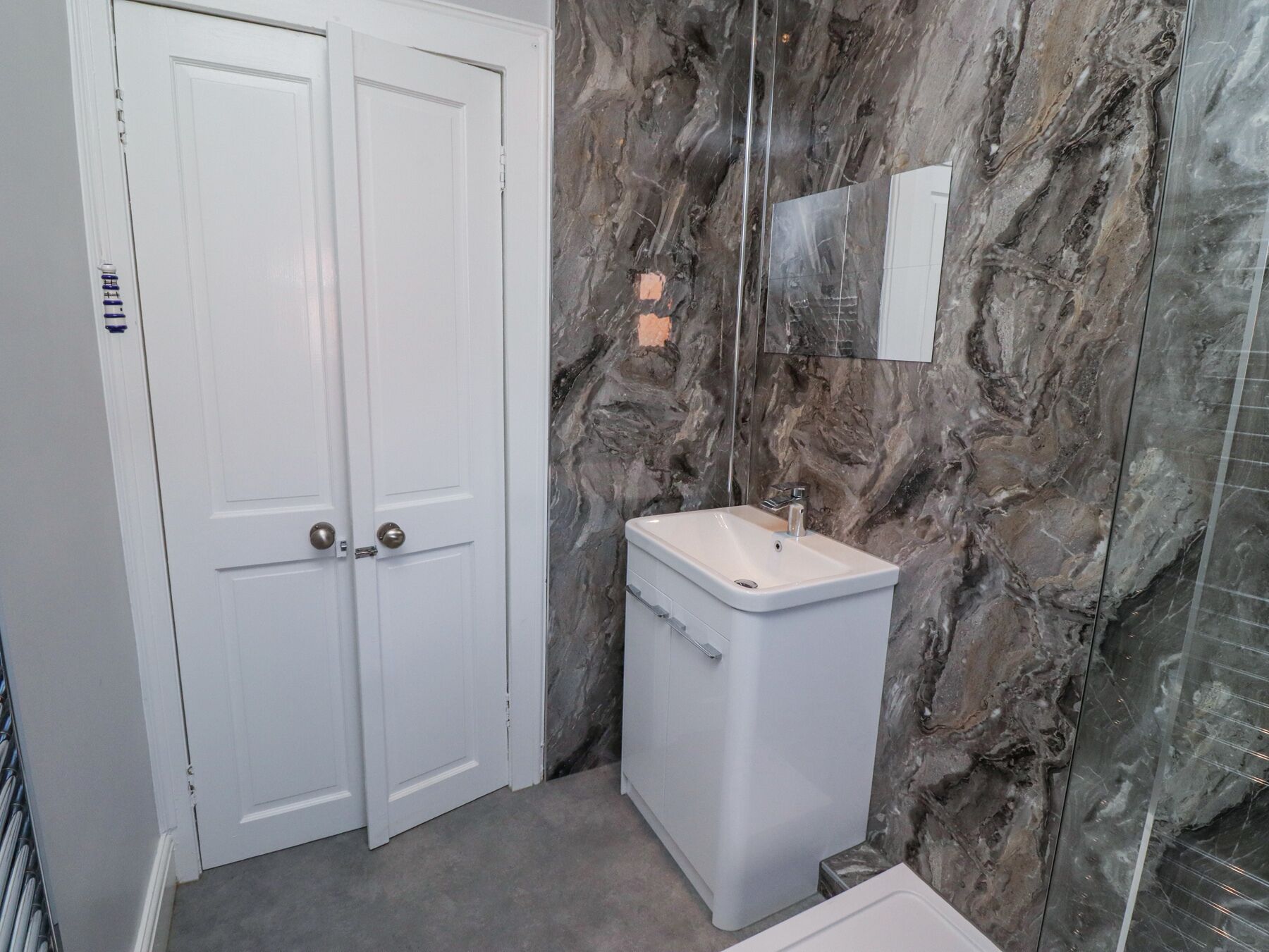 Un baño con pared de mármol, un lavabo blanco y una puerta doble.