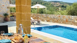 An outdoor dining area with a pool, stone walls, and a view of a hillside. - Stunning Family sea view Villa with private pool (Stoupa)