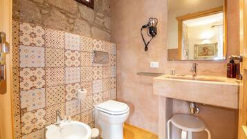 Een badkamer met een wastafel, toilet en een douchetoilet. De muren zijn betegeld met een decoratief patroon.