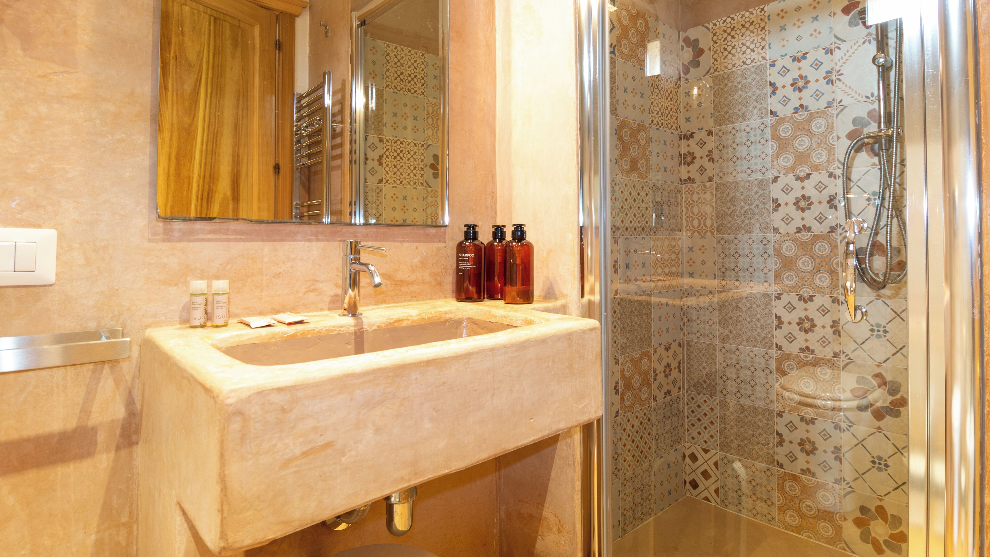Un baño con lavamanos de mármol, un espejo y una ducha con azulejos estampados.