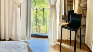 A bedroom with a balcony, white curtains, a bed, and a chair. - Bosa Eye House 1873 (Bosa)