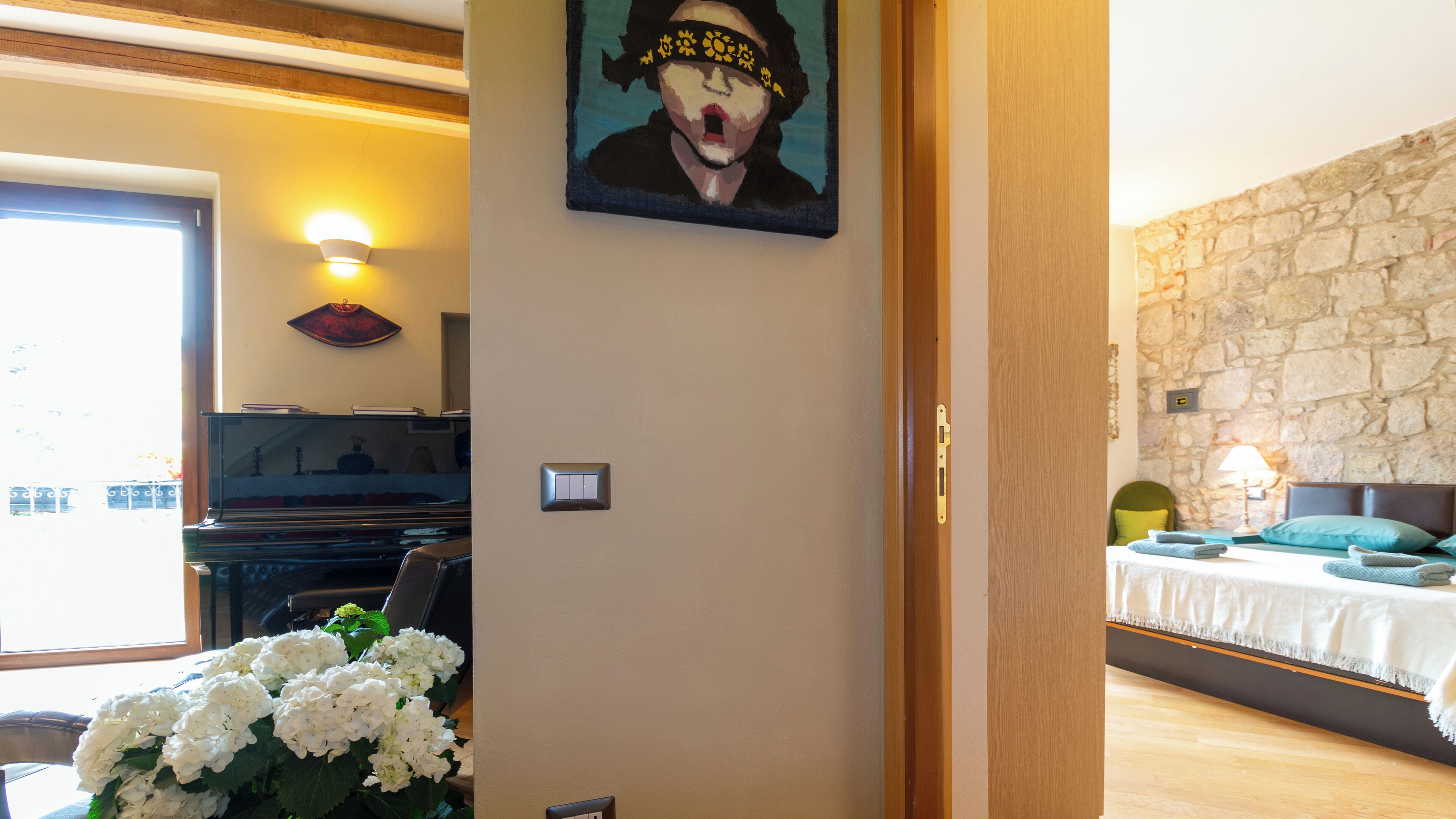 Una habitación con un piano, un cuadro, una cama con almohadas y una pared de piedra.