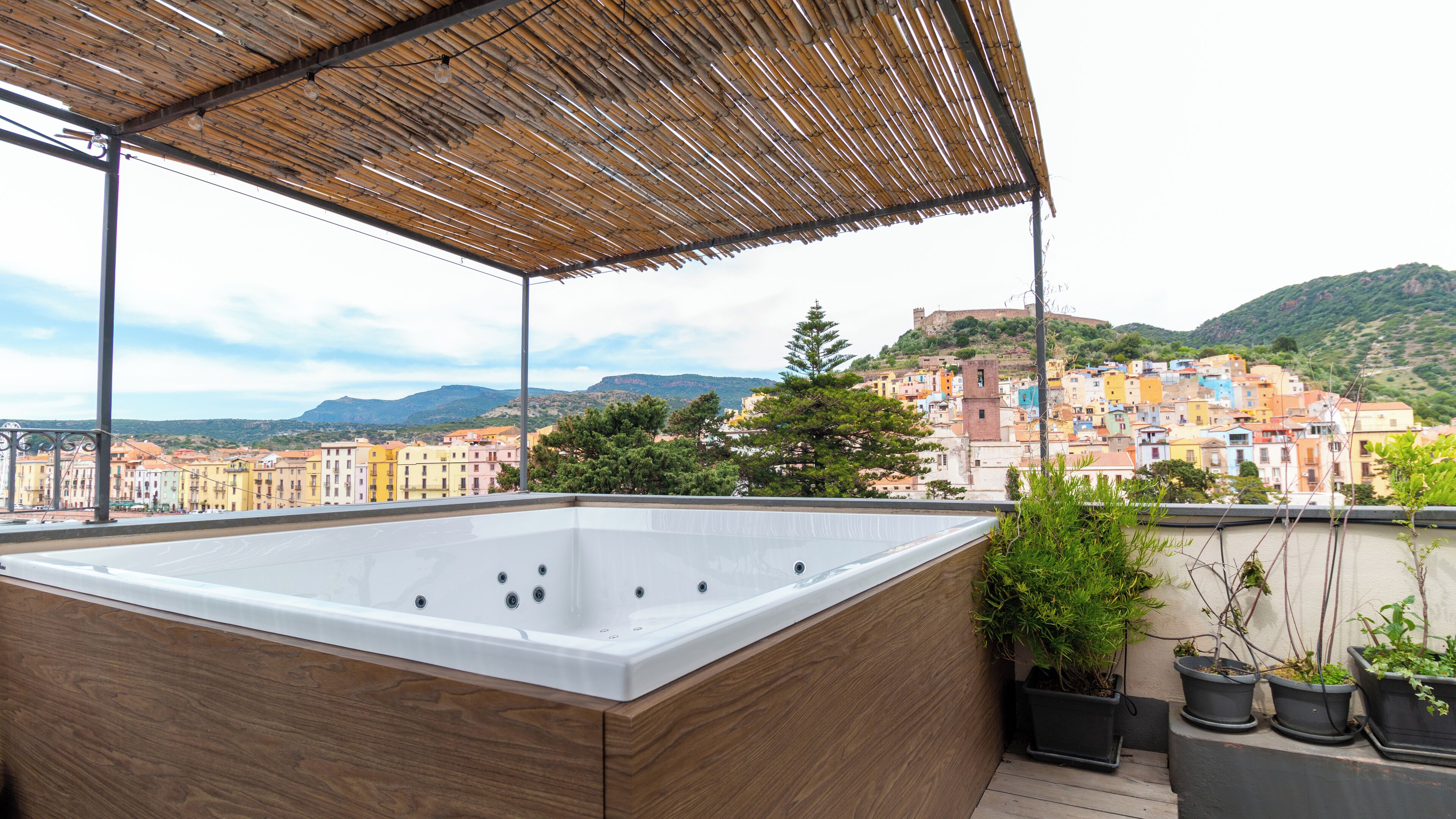 A rooftop with a wooden deck, a hot tub, and potted plants.