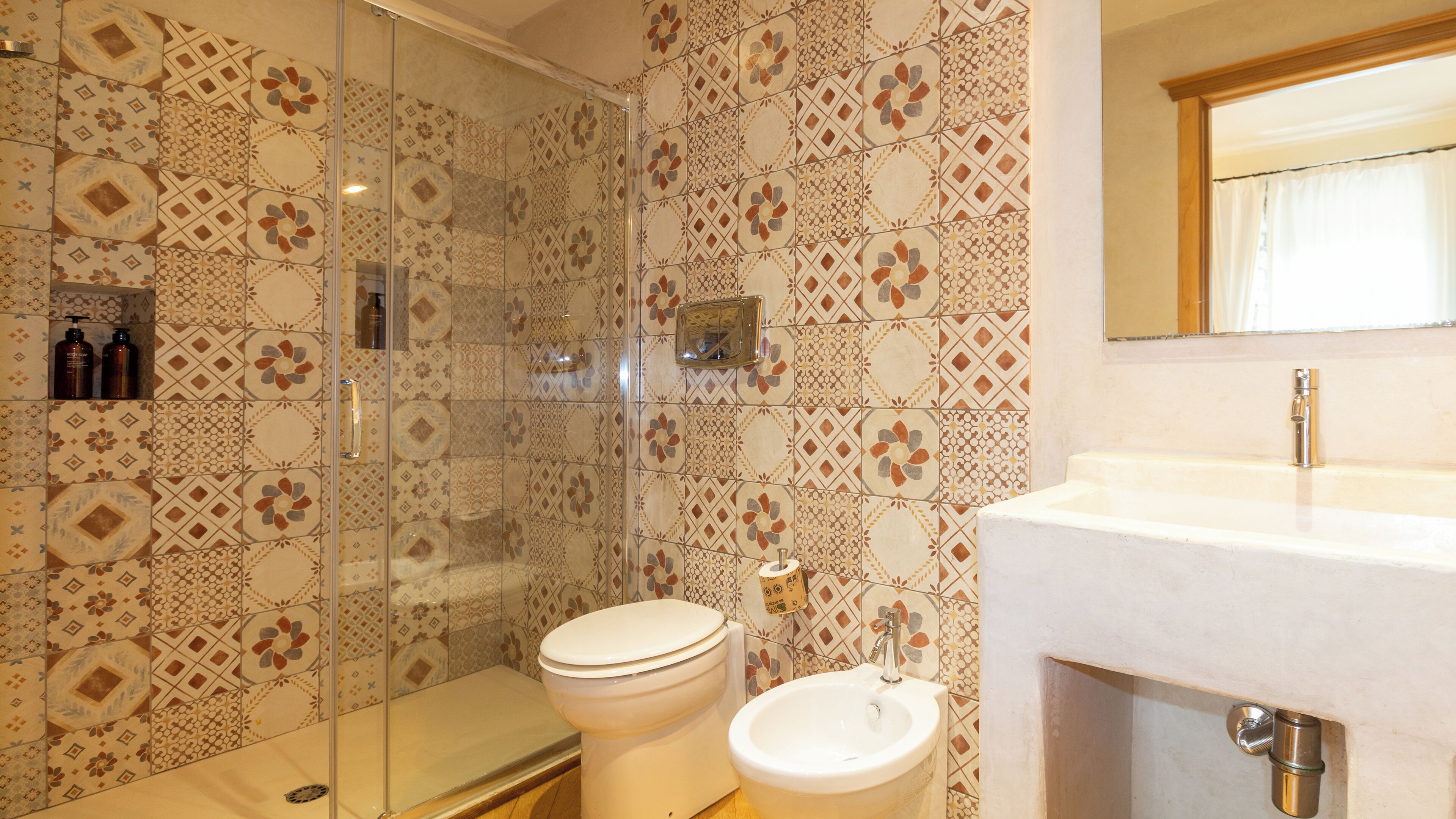Une salle de bain avec des carreaux décoratifs, une douche en verre, des toilettes et un lavabo avec un miroir au-dessus.