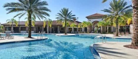 A swimming pool with clear water, surrounded by palm trees and a building with a tiled roof.