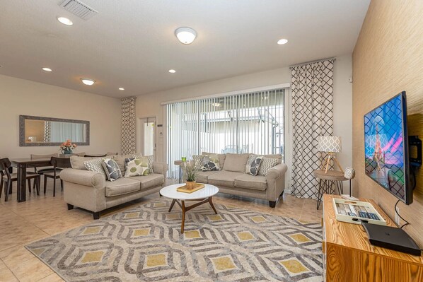 A living room with two sofas, a coffee table, a TV, and a dining area with chairs and a table.