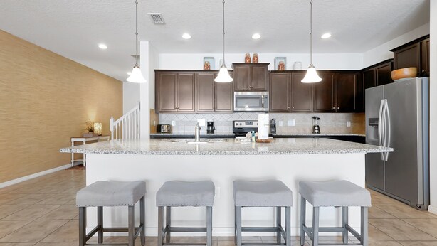 A modern kitchen with a large island, stainless steel appliances, and pendant lighting.