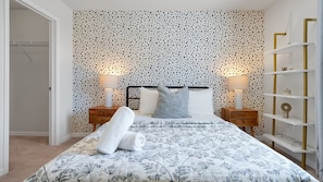 A bedroom with a patterned bedspread, two bedside tables with lamps, a headboard, and a shelving unit. - 7BR Solterra Villa | Private Pool & Spa | Mickey Room | Near Disney (Davenport)