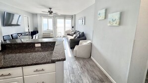 Una cocina moderna con encimeras de granito, una zona de comedor con mesa y sillas, un sofá gris y un ventilador de techo.