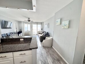 A modern kitchen with granite countertops, a dining area with a table and chairs, a gray sofa, and a ceiling fan.